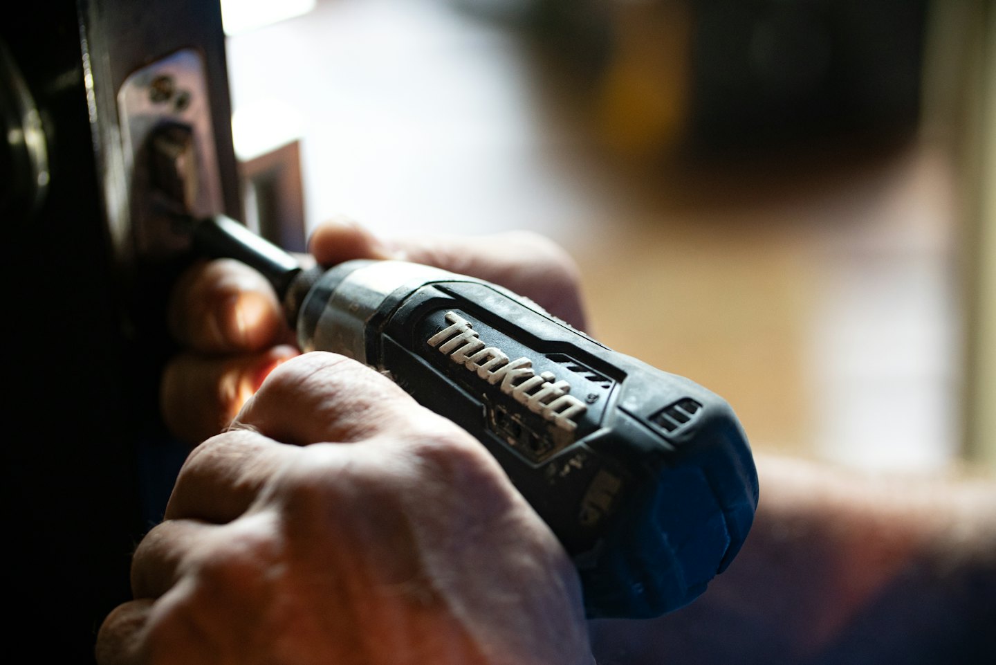 Hands using a Makita power screwdriver to install a screw.